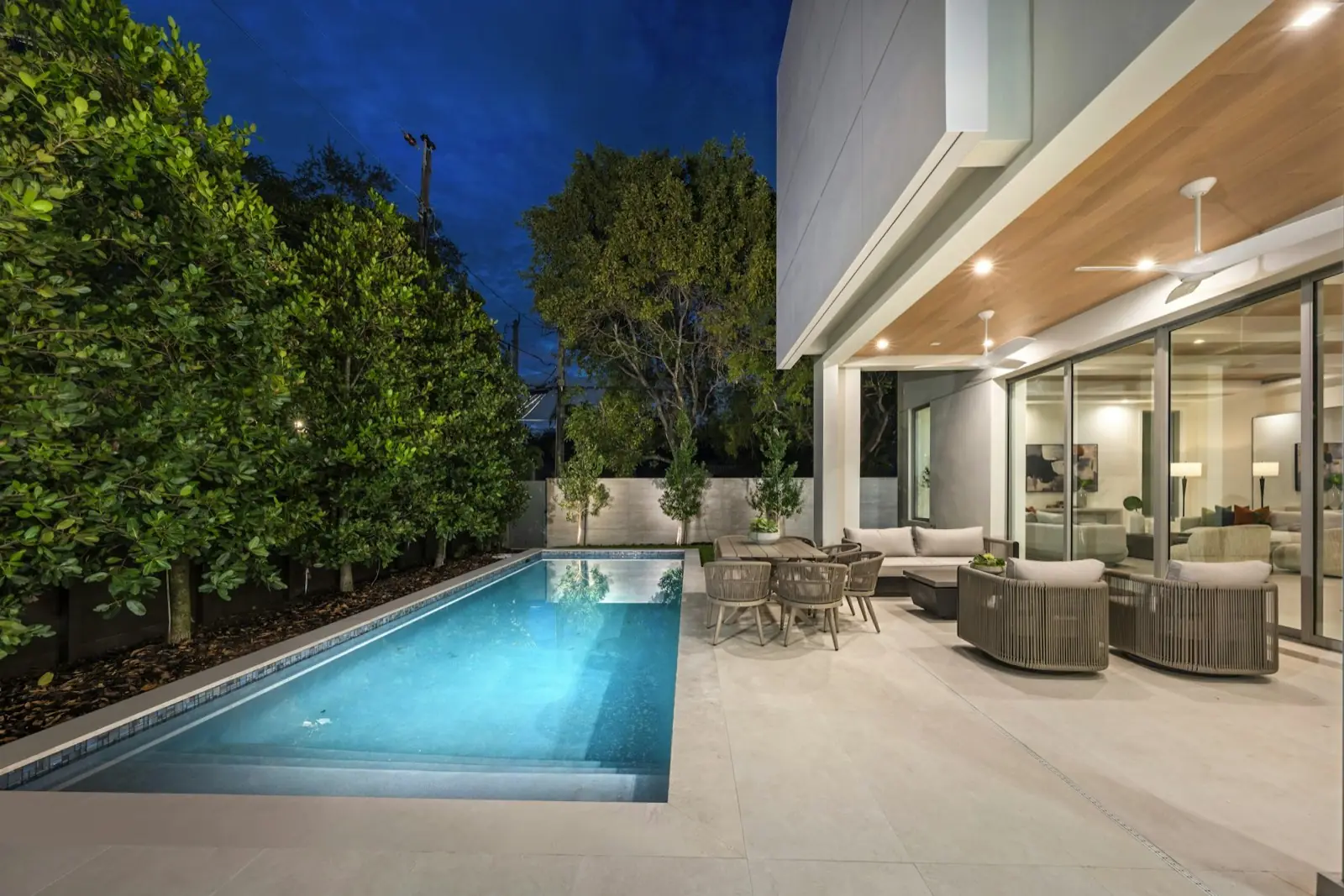 Modern backyard at night with large grey pavers, lit pool, lounge area and landscape lighting